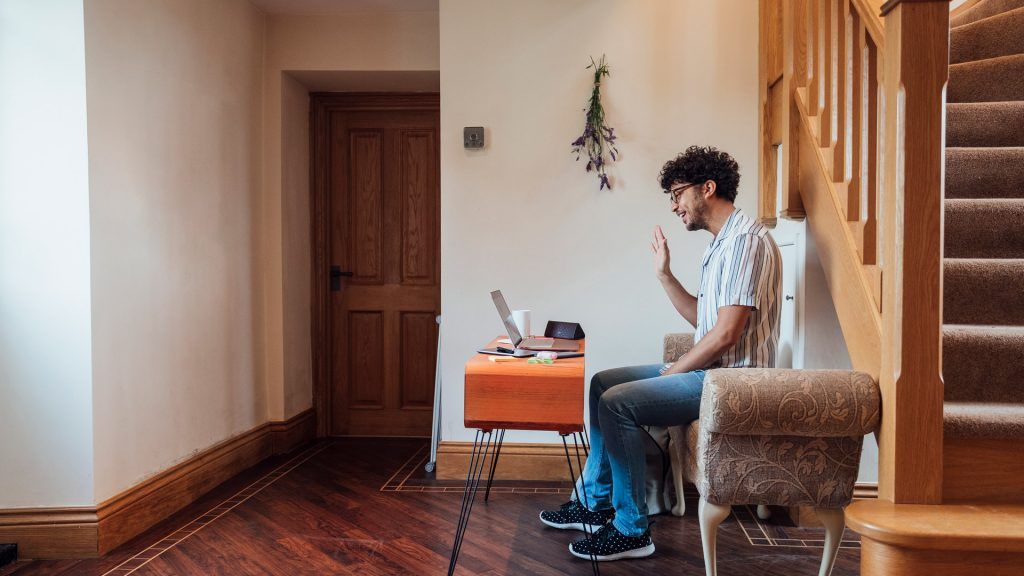 Person sitting on a couch waving at his laptop, attending an online sobriety group